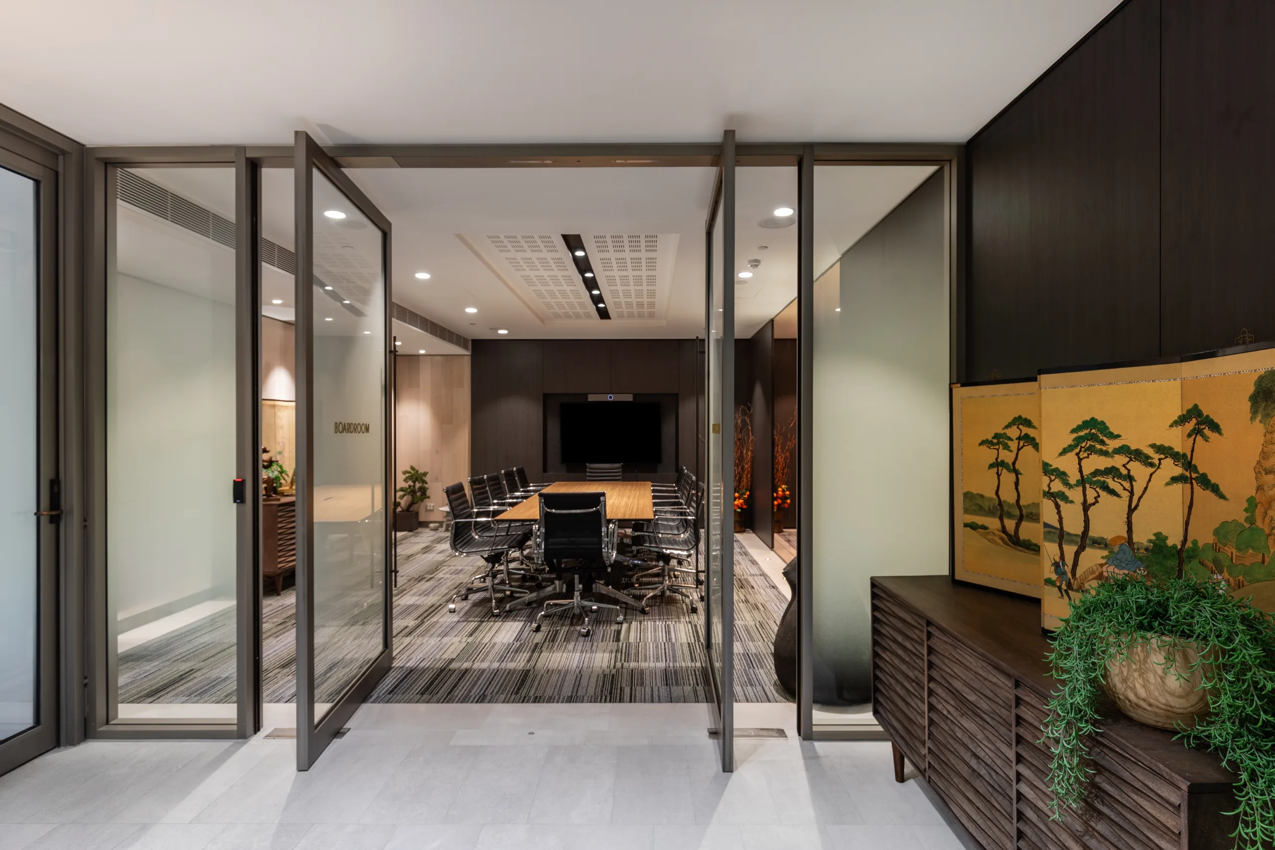 Glass doors open to a modern boardroom featuring a long wooden table and black ergonomic chairs.