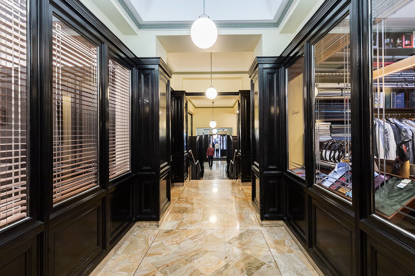 A bright hallway with marble floors, black wood-panelled walls, and large glass windows under hanging globe lights.