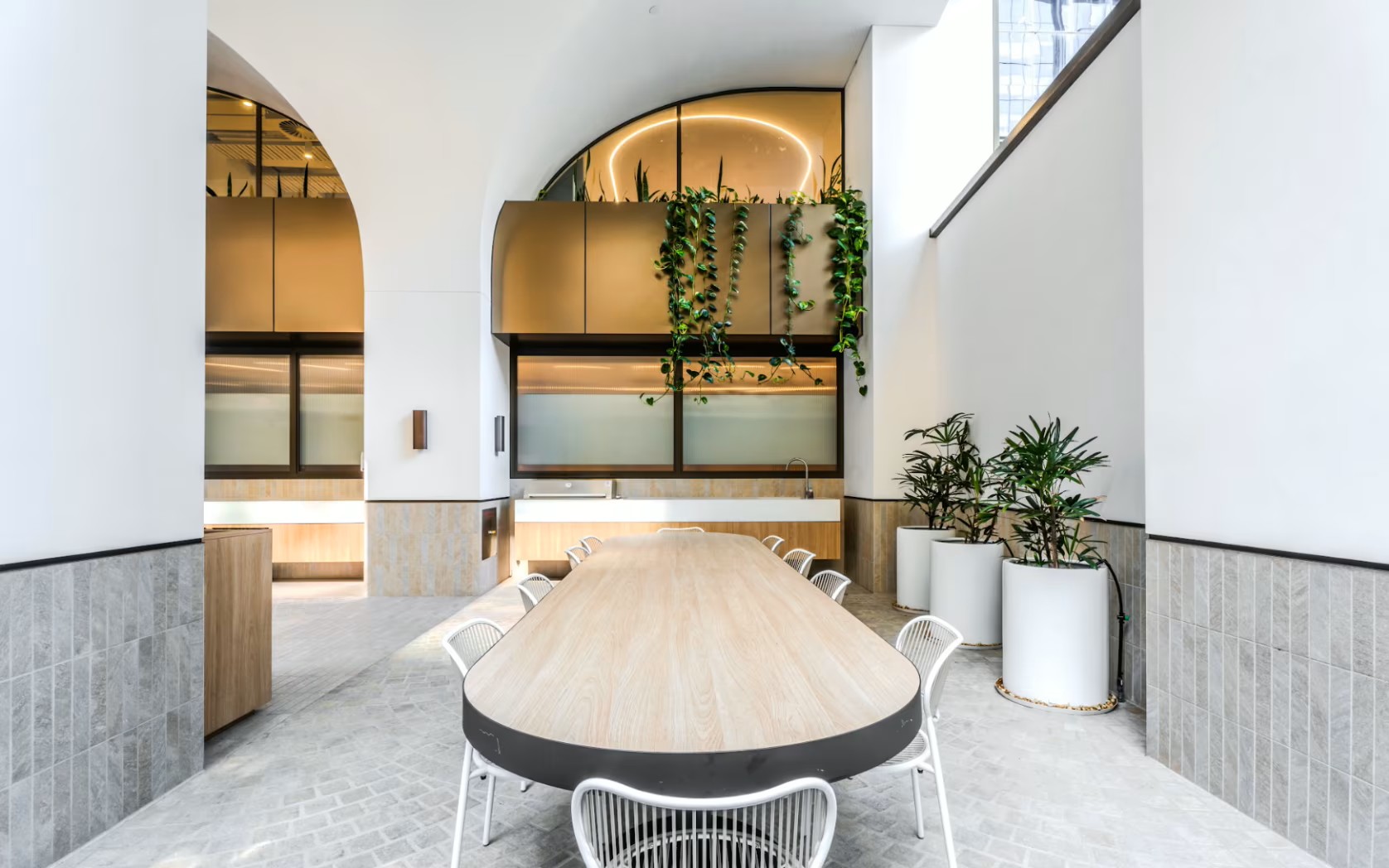 Bright, modern office breakout area featuring a long wooden table, white chairs, and indoor plants.
