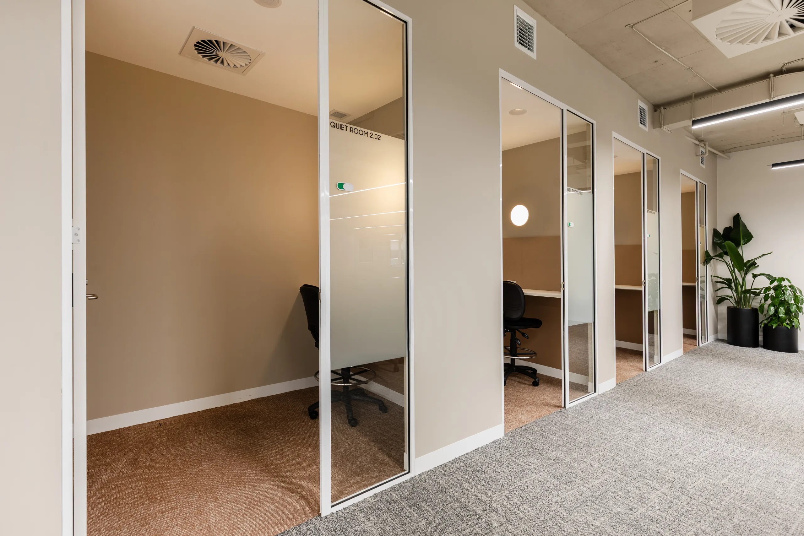 A row of private quiet rooms with glass doors and carpeted floors in a bright office space.