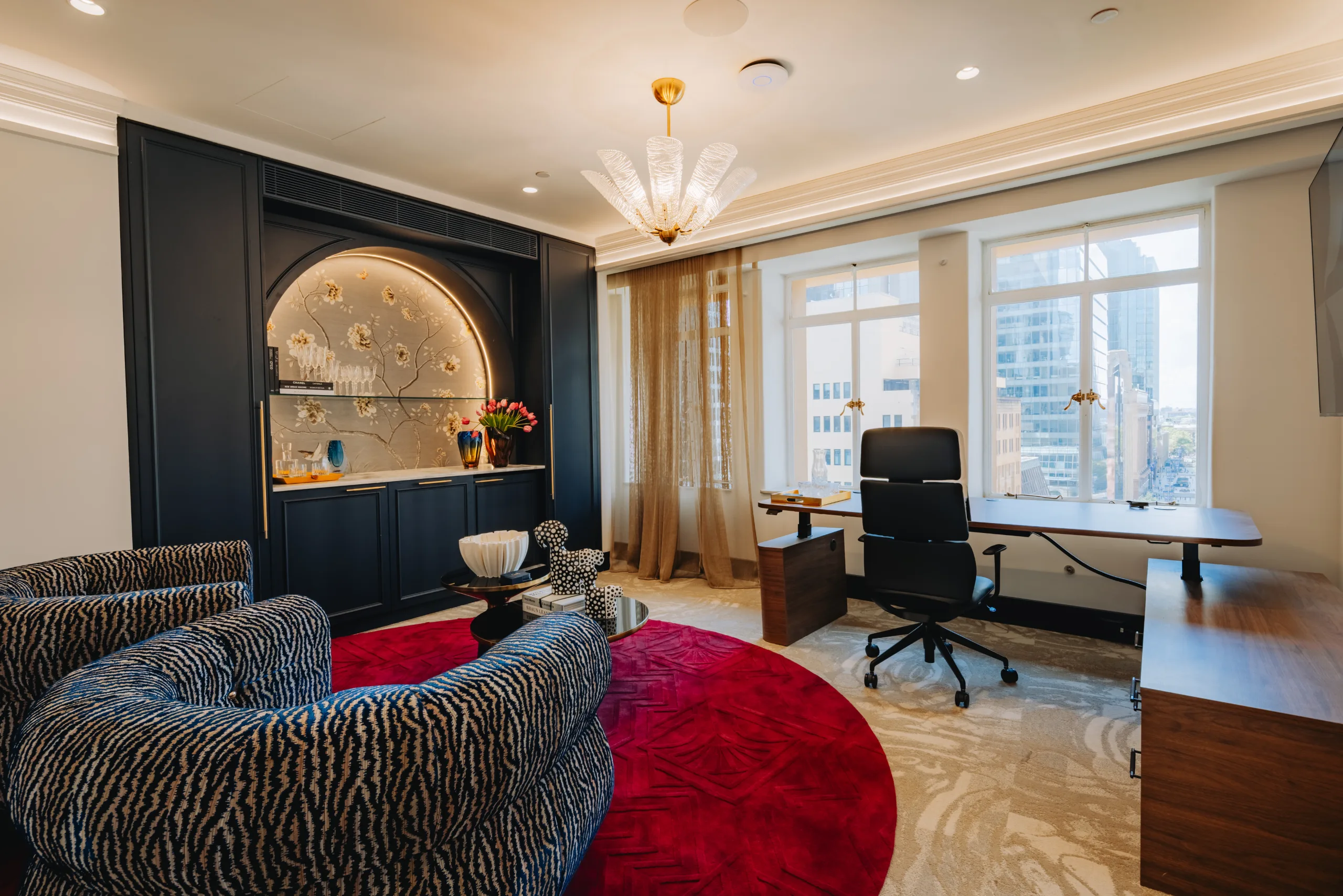 Modern office featuring a large wooden desk, patterned armchairs, and large windows with bright natural light.