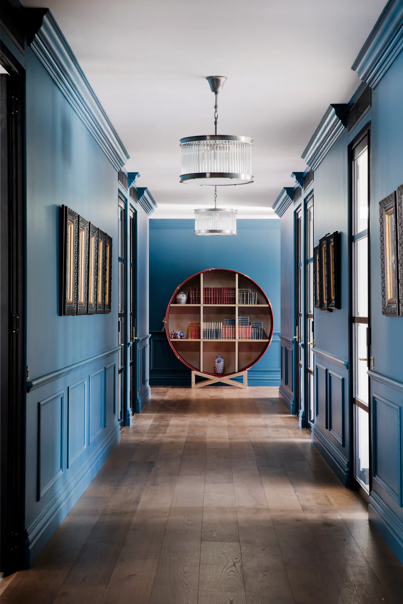 A long blue hallway features wooden floors, decorative wall paneling, and two large glass pendant lights.
