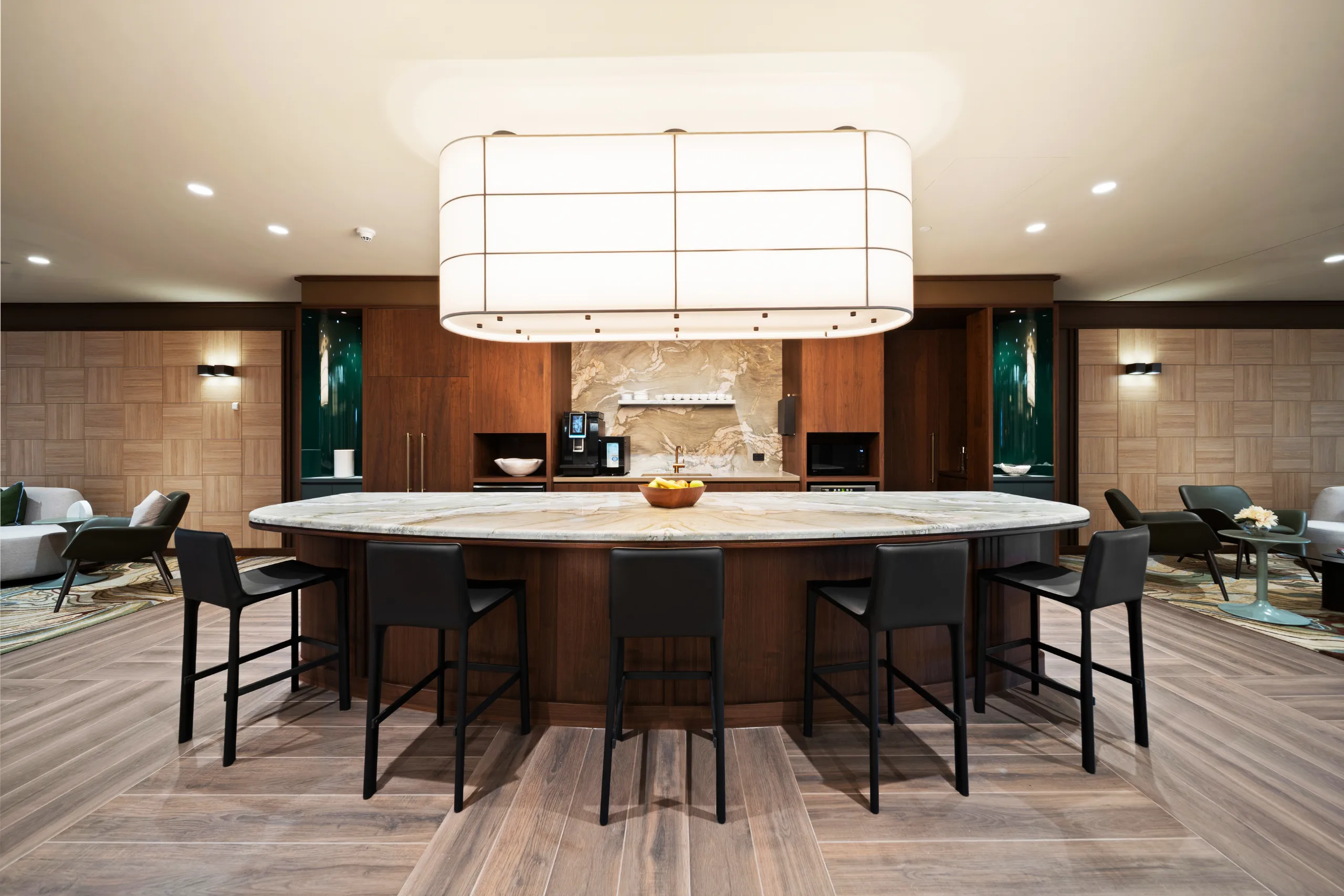 Modern office lounge featuring a large marble communal table with black bar stools and warm ambient lighting.
