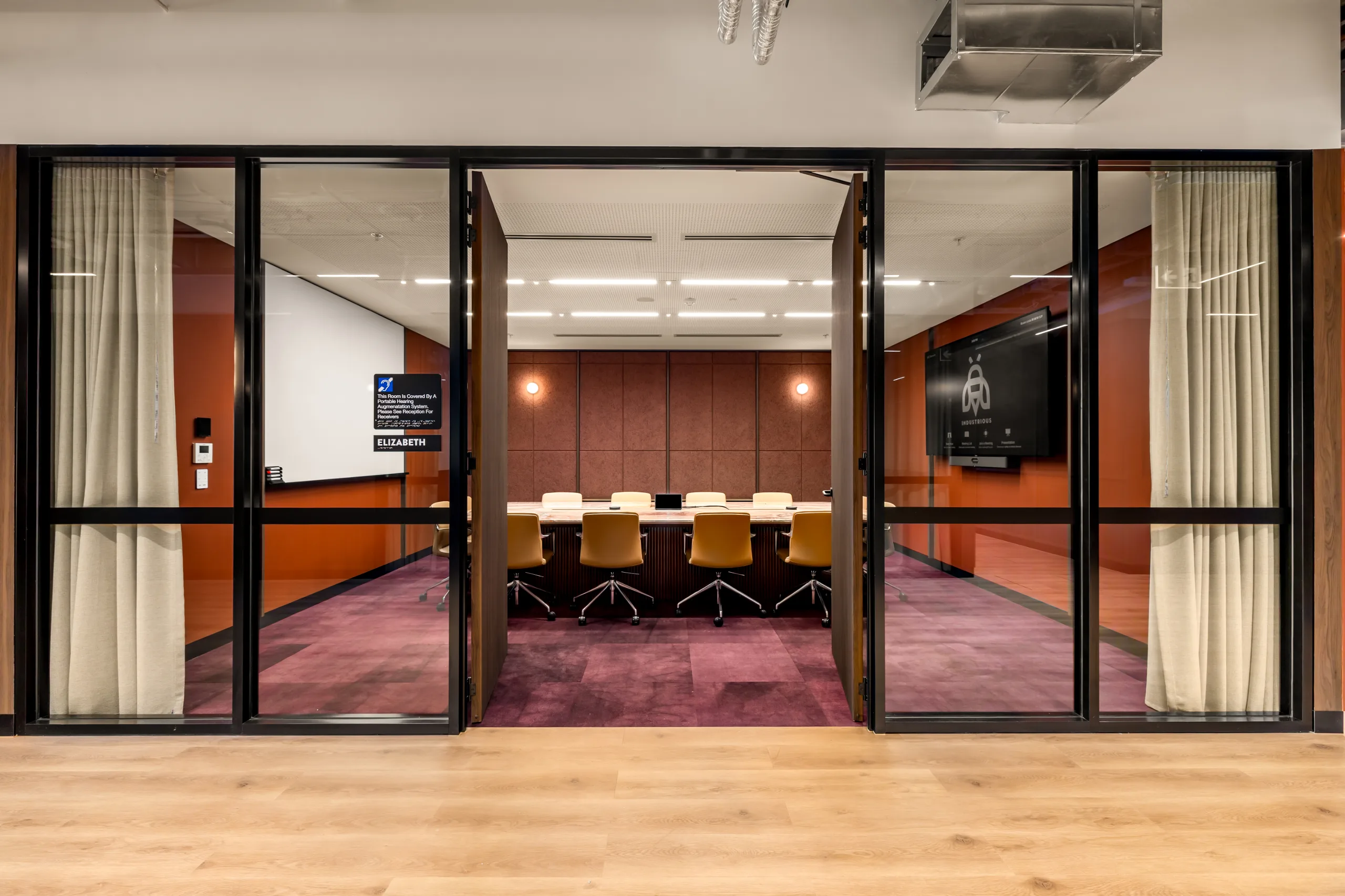 Modern conference room with a long wooden table, orange walls, and large glass doors.
