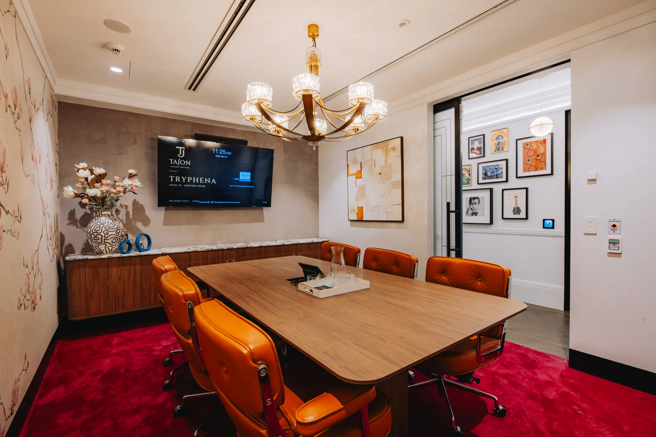 Modern meeting room featuring a large wooden table, orange leather chairs, and a bright chandelier.