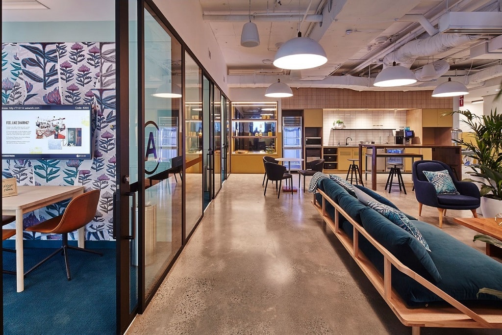 Modern office lounge with a long blue sofa, polished concrete floors, and glass-walled meeting rooms.