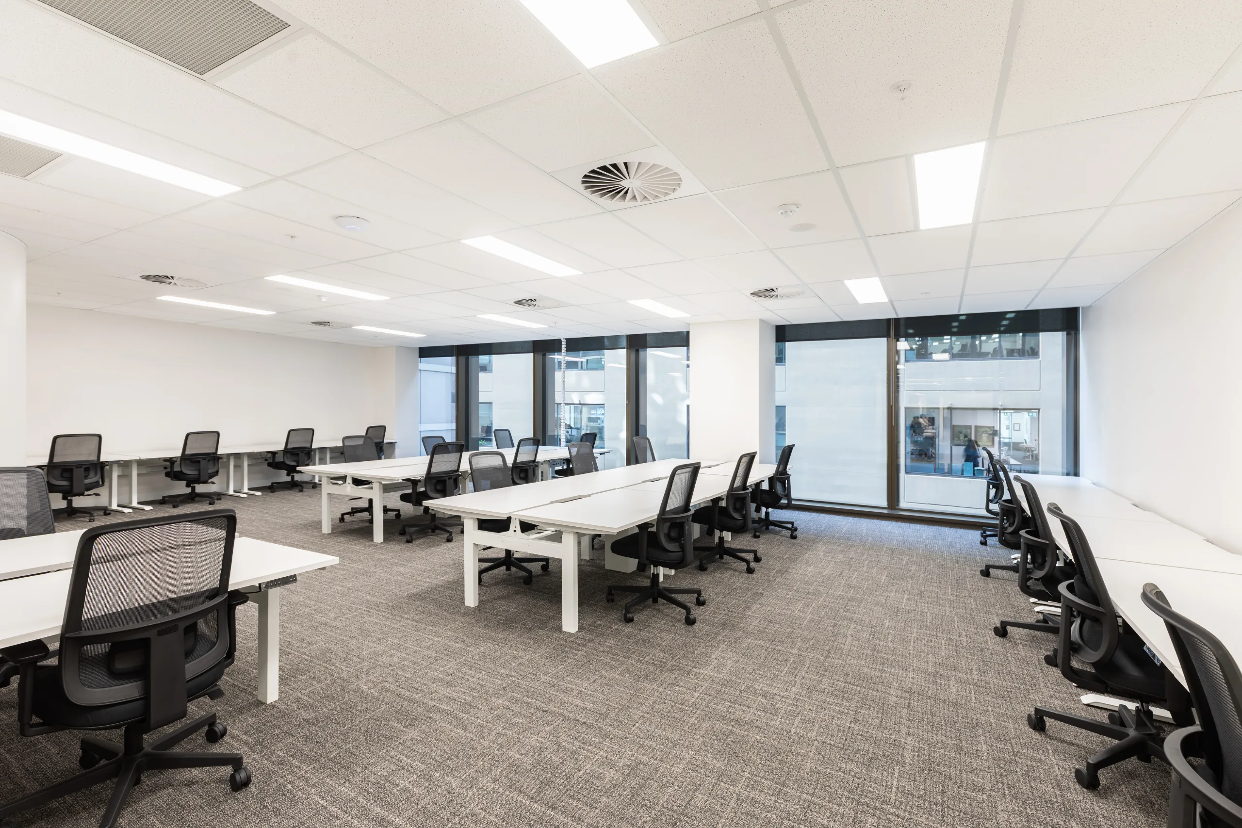 Bright, modern open-plan office space with white desks, black ergonomic chairs, and large windows.