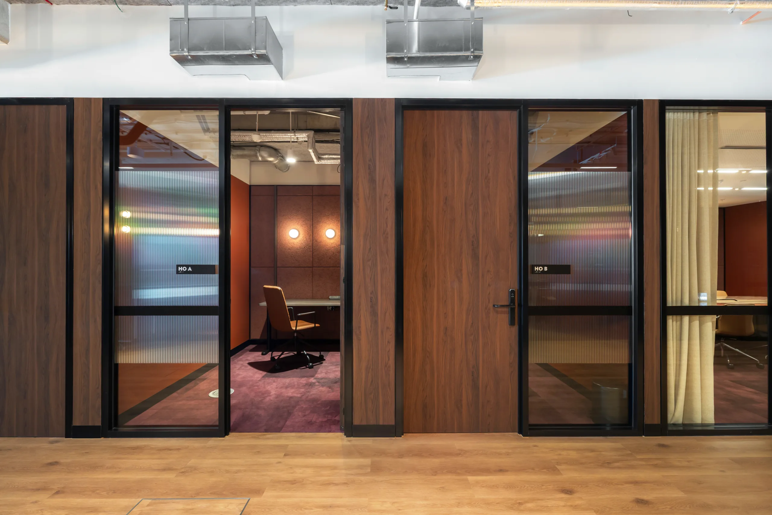 Modern office meeting rooms with dark wood paneling, glass doors, and warm interior lighting.