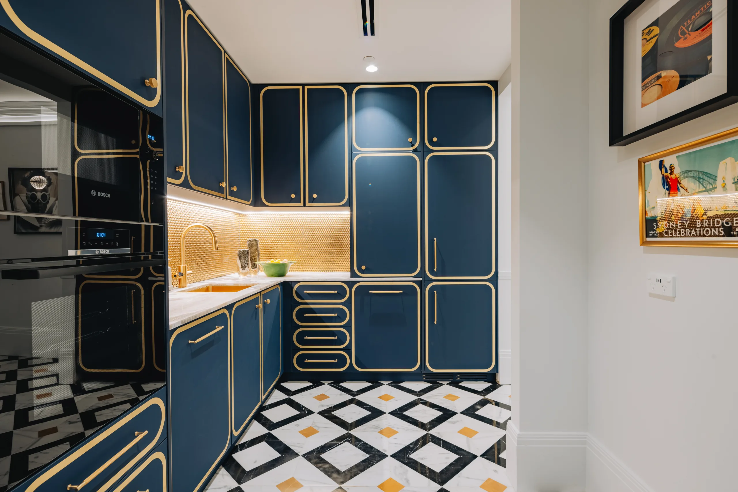 Modern kitchenette featuring navy blue cabinetry with gold trim and patterned black and white floor tiles.