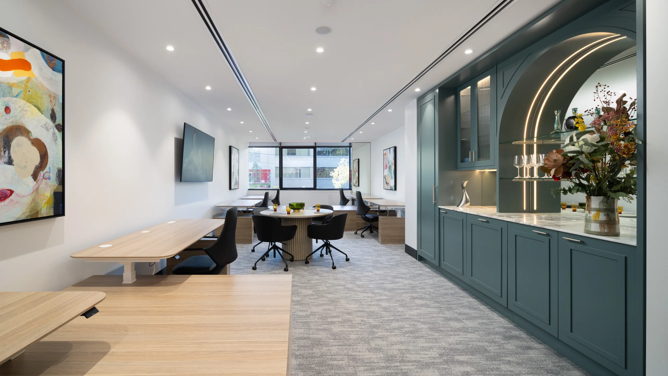 Modern office space featuring wooden desks, a round meeting table, and built-in teal cabinetry with bright lighting.