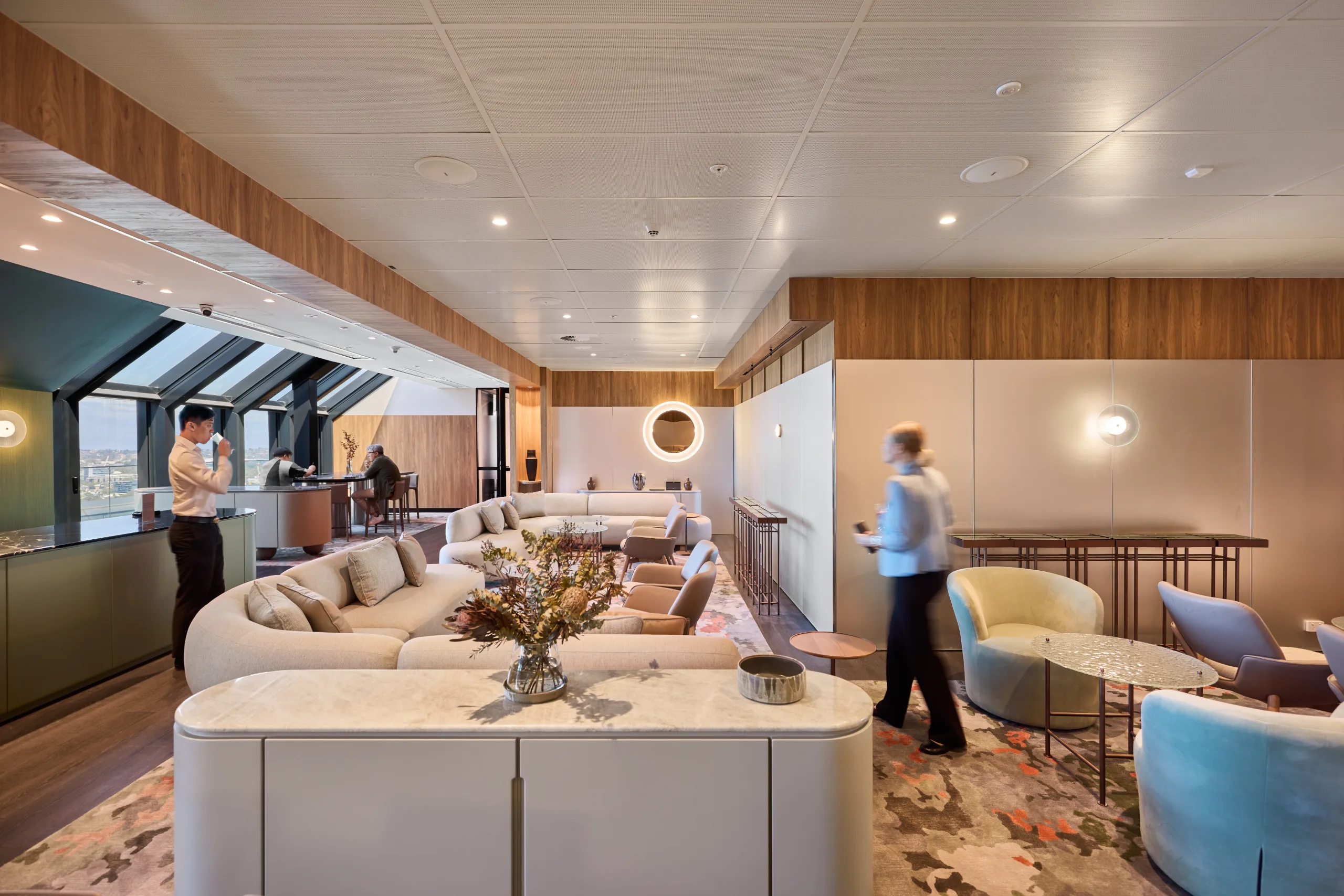 Bright, modern lounge area with soft seating, wooden accents, and large windows overlooking a distant landscape.