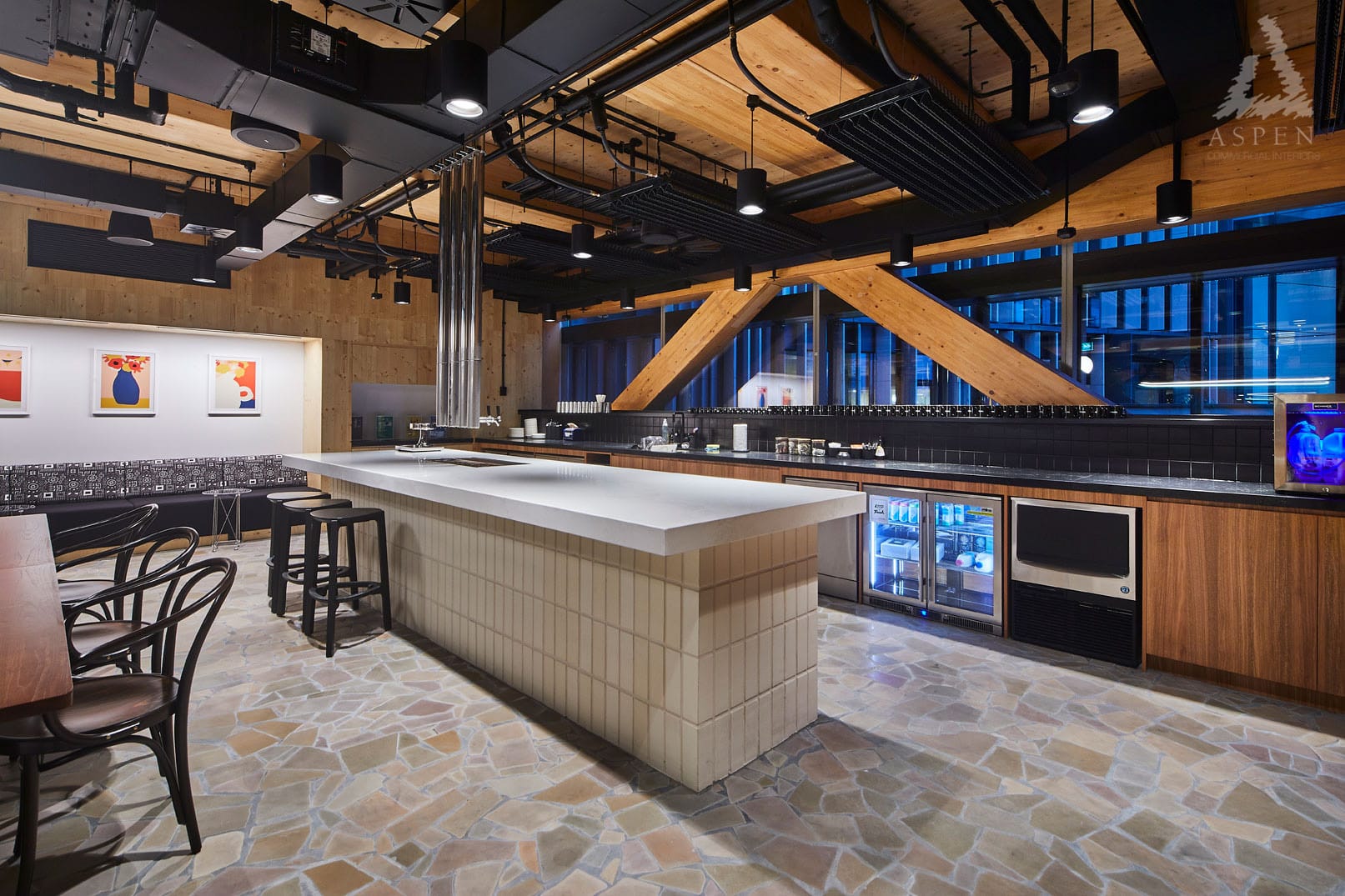 Modern office kitchen area featuring a large white island, wooden cabinetry, and large windows with city views.