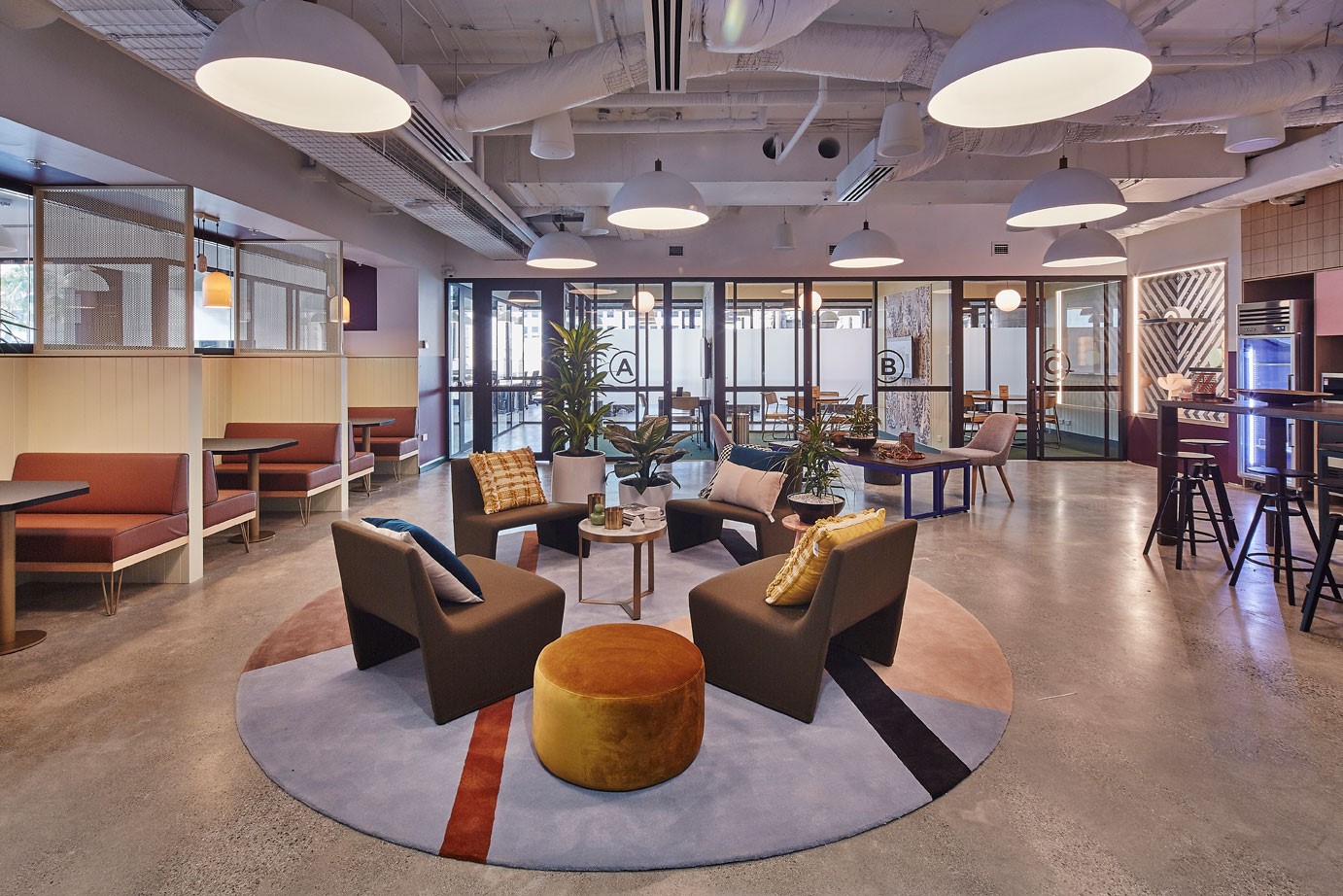 Modern office lounge featuring colourful armchairs, a circular rug, and bright pendant lighting in an open space.