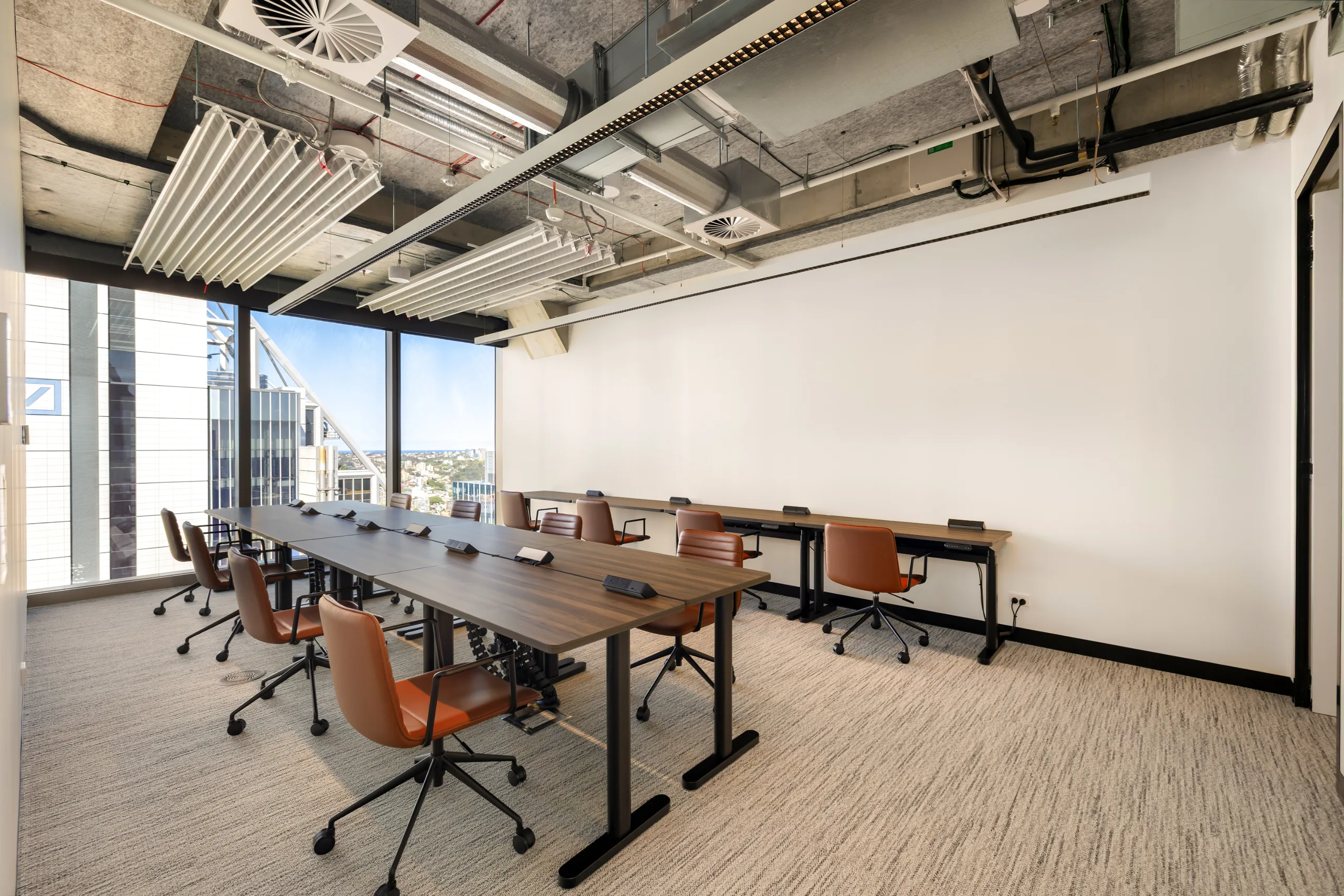 Modern conference room featuring a long dark table, leather chairs, and large windows with city views.