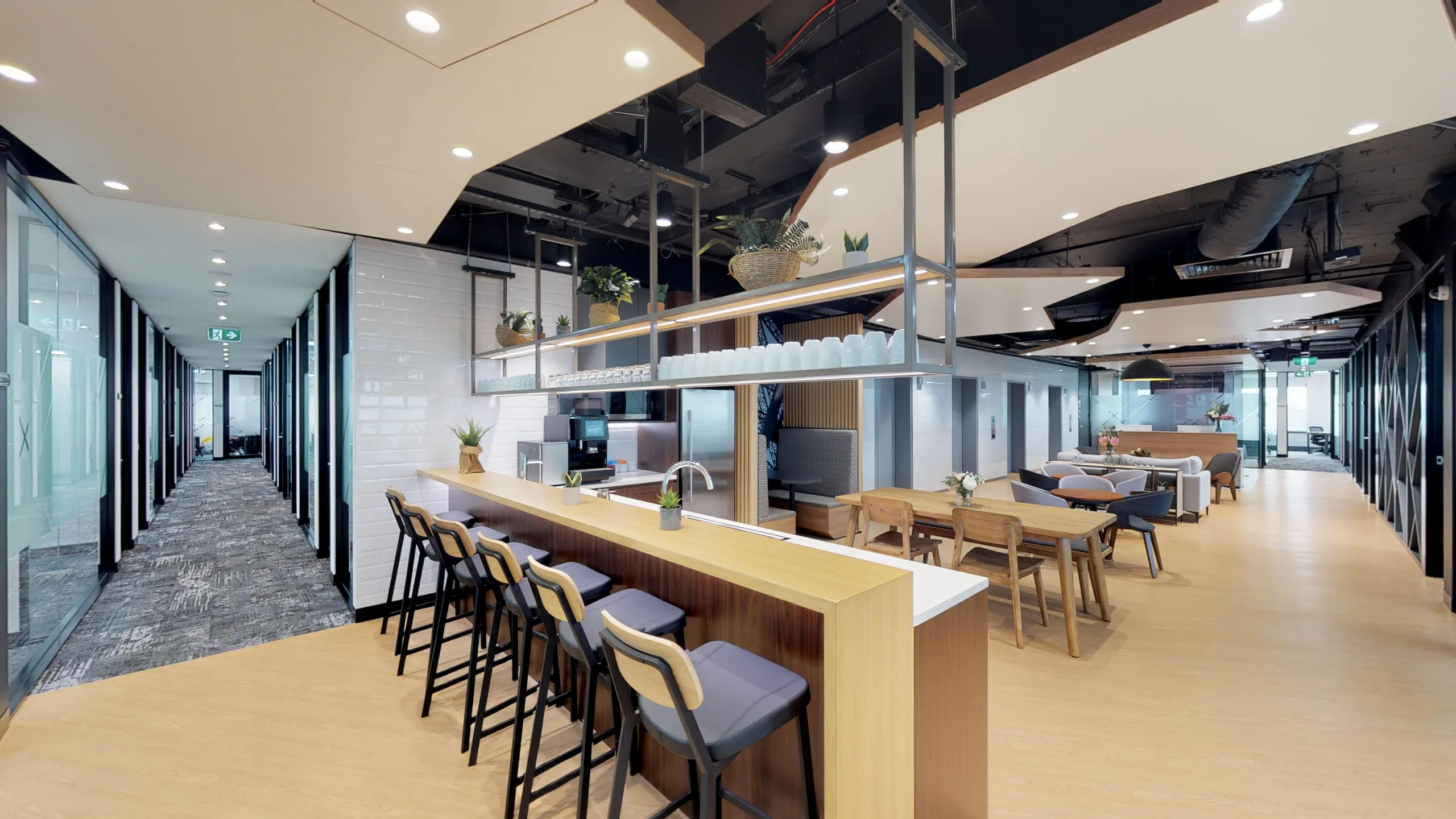 Modern open-plan office featuring a long wooden breakfast bar, lounge seating, and bright, contemporary lighting.