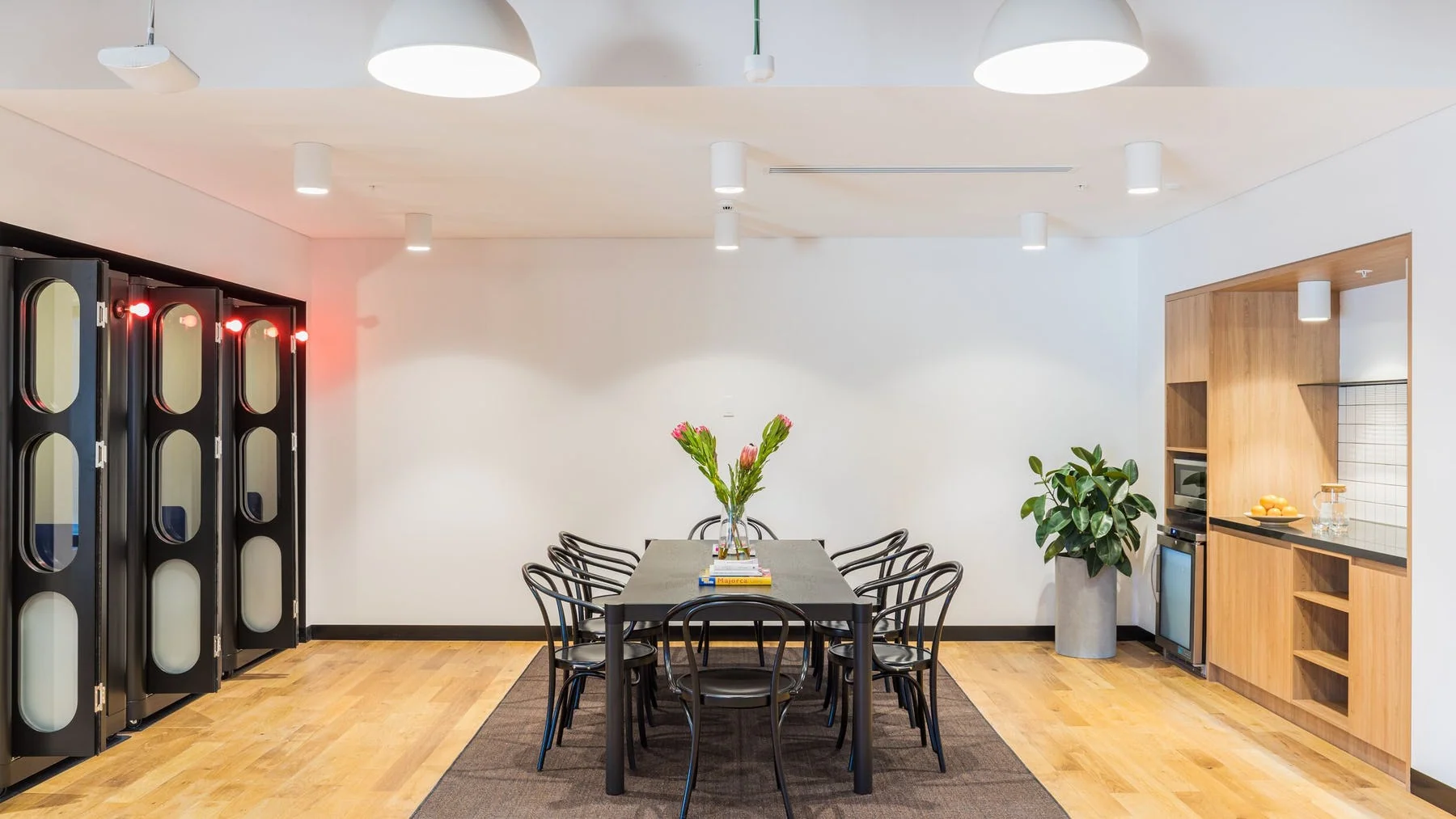 Brightly lit meeting room featuring a long black table, several chairs, and large glass-paned doors.