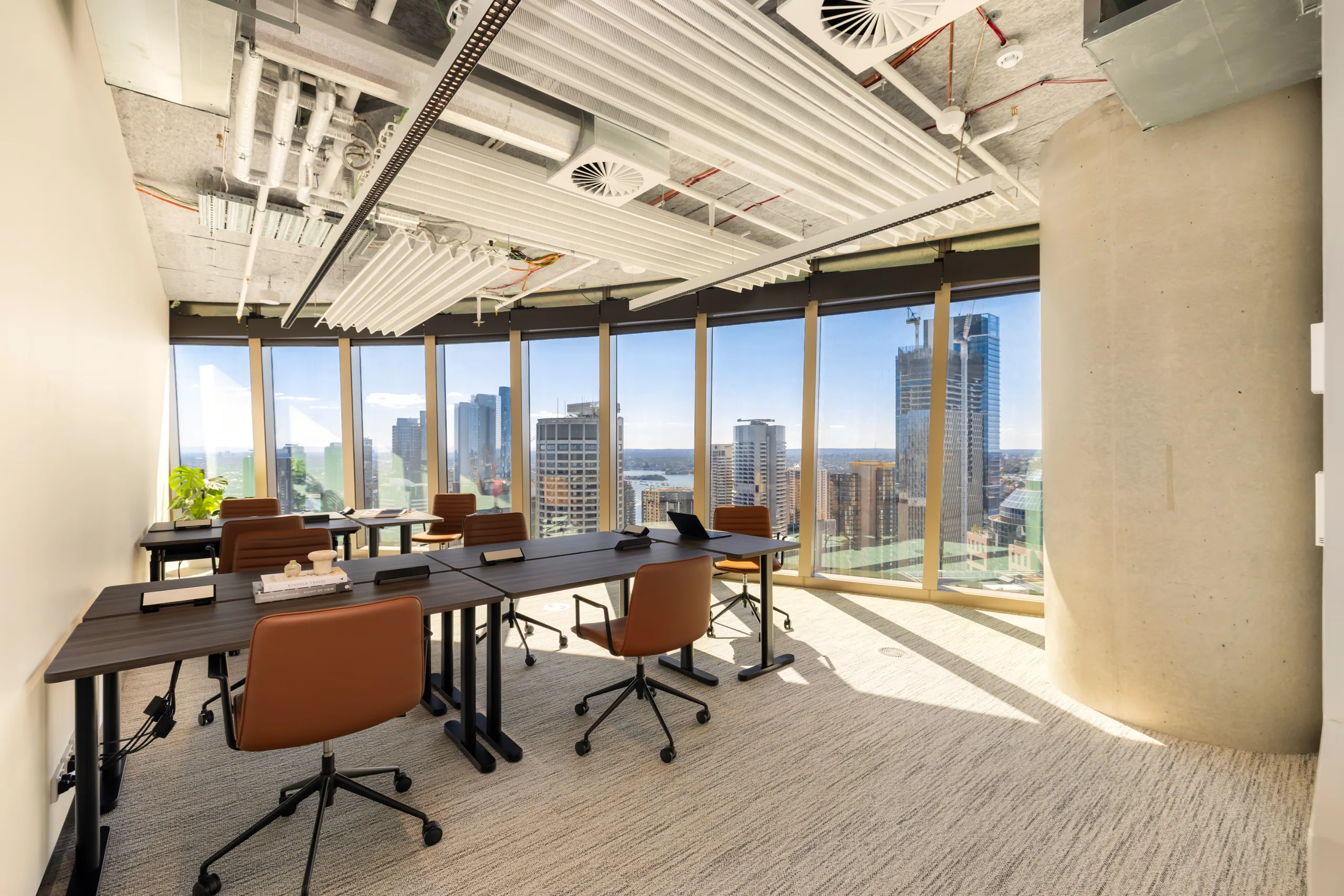 Bright, modern office space with dark desks, brown chairs, and large windows overlooking a city skyline.