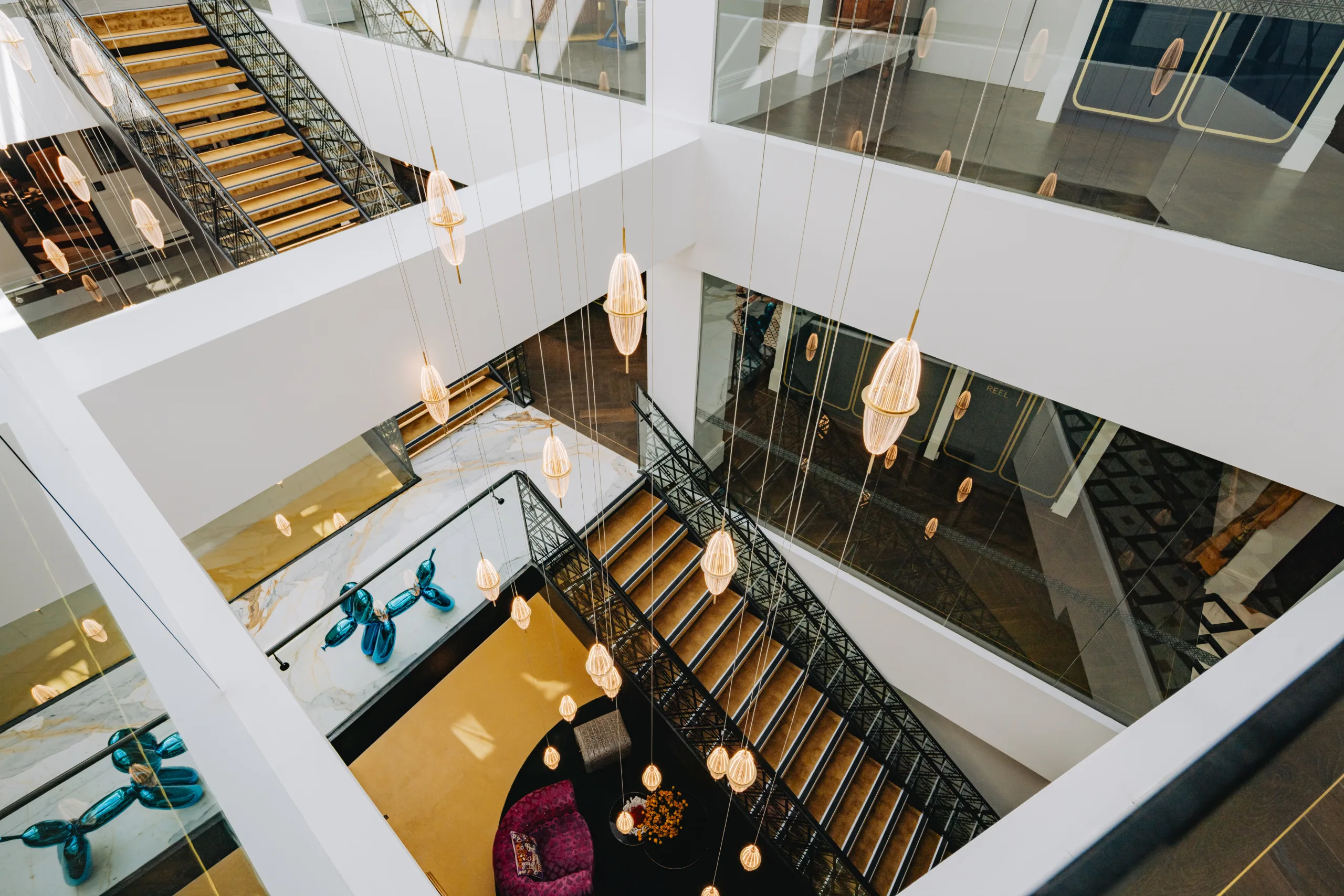 Modern multi-level office atrium featuring hanging pendant lights, black metal staircases, and bright, natural light.