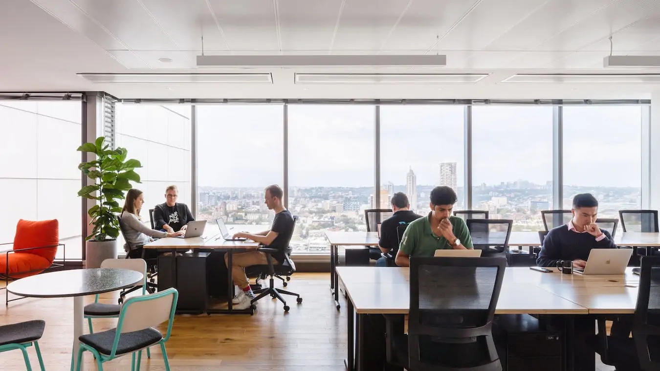 Bright, modern open-plan office with large windows overlooking a city skyline and natural light.