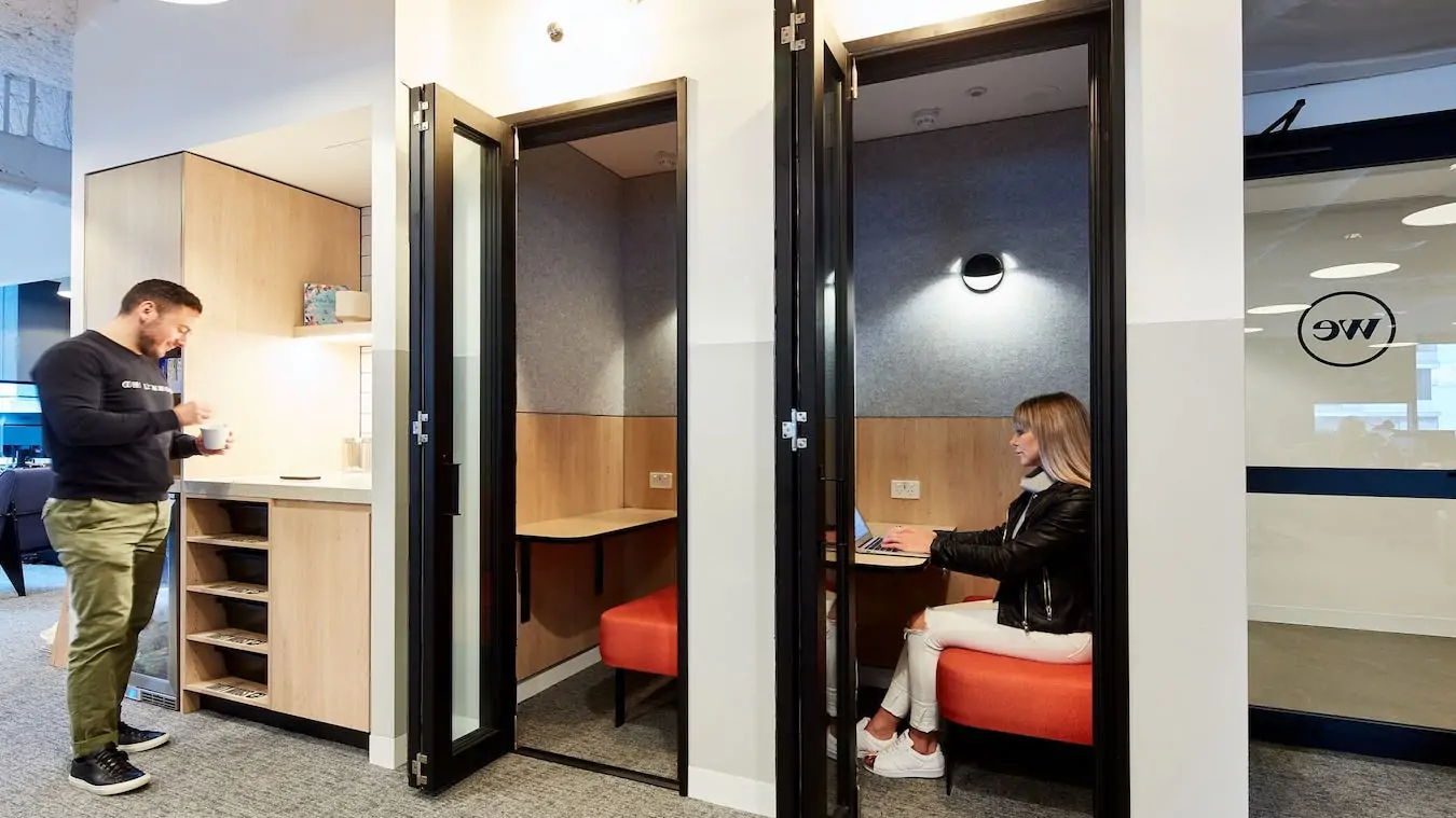 Bright office space featuring private phone booths with wooden desks and orange seating.