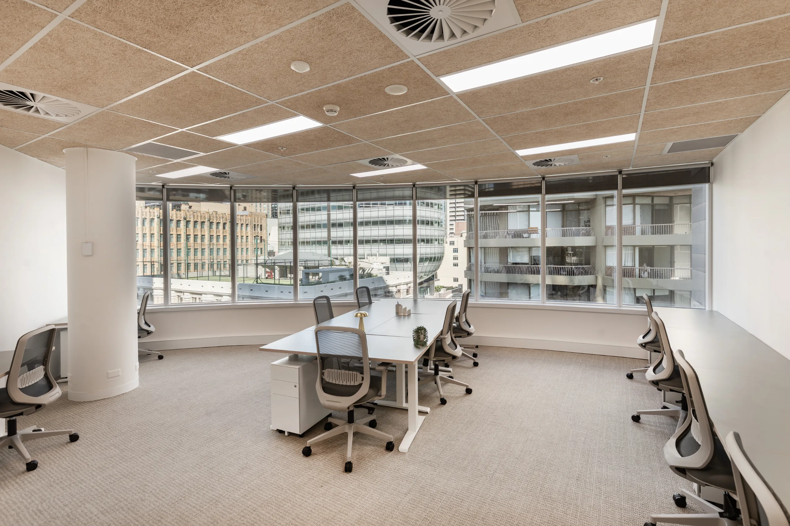 Bright, modern office meeting room with a large table, ergonomic chairs, and large windows overlooking city buildings.
