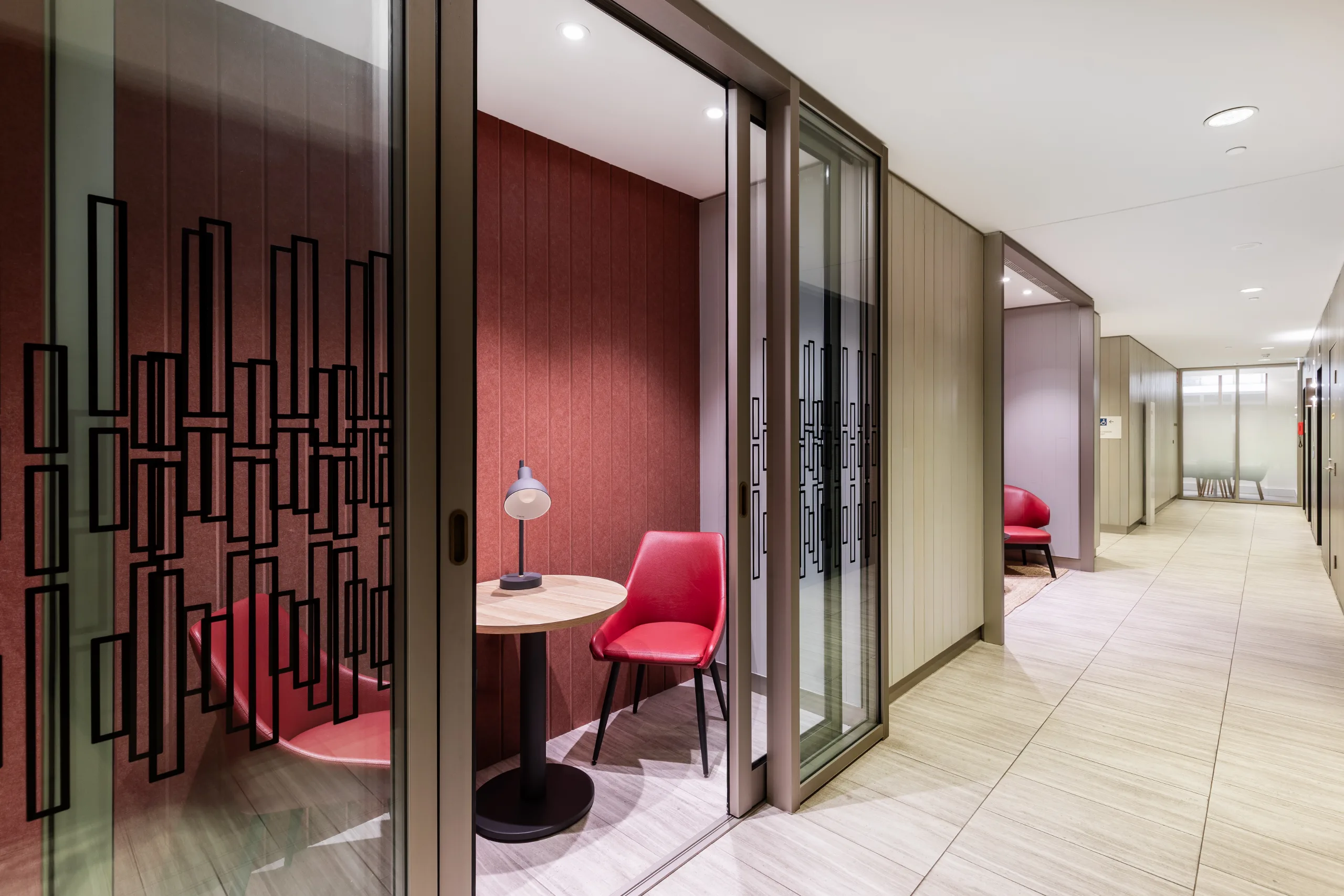 Small private meeting room with red walls, a round table, a red chair, and a desk lamp.
