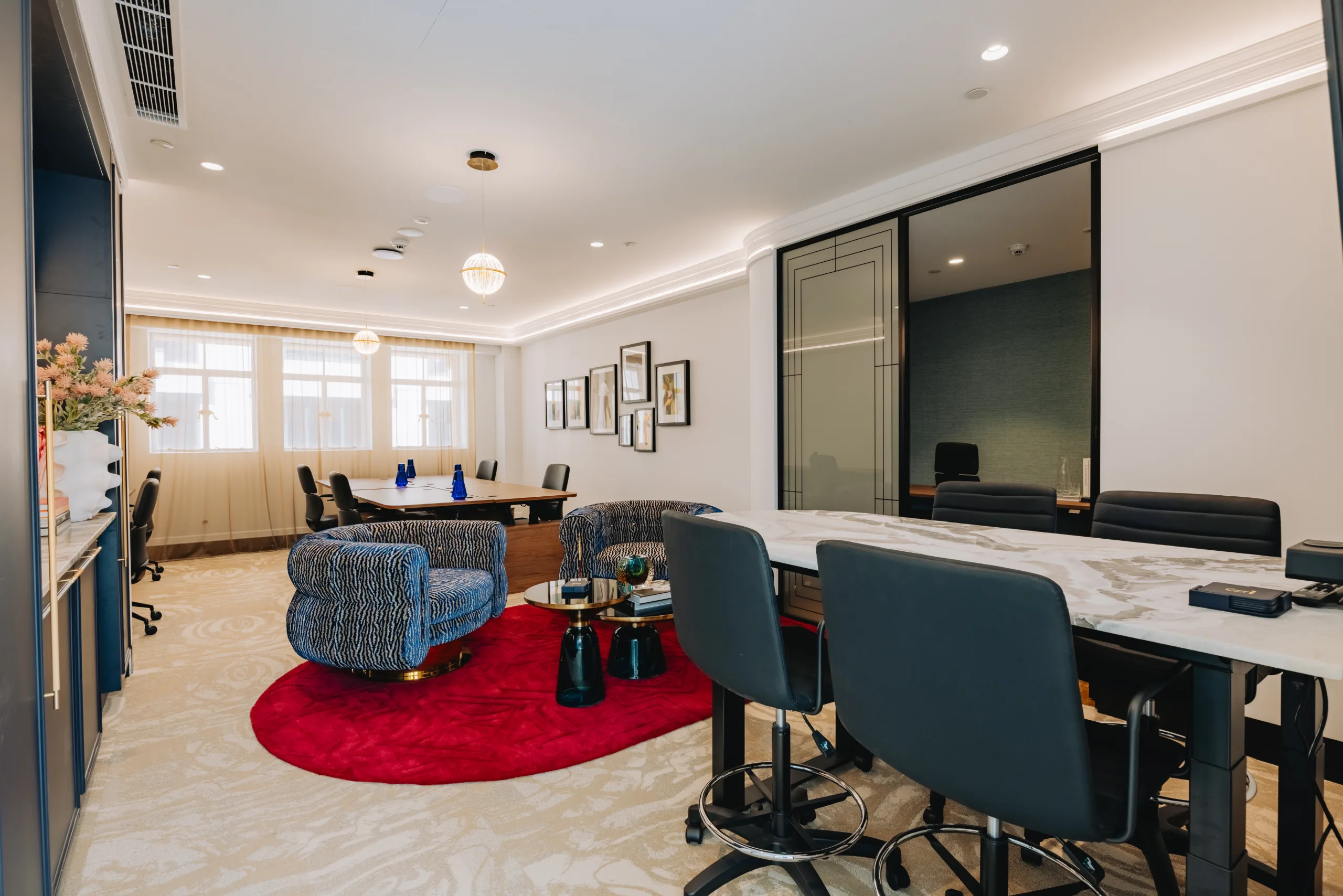 Bright, modern office lounge featuring a marble table, blue armchairs, and a large red circular rug.