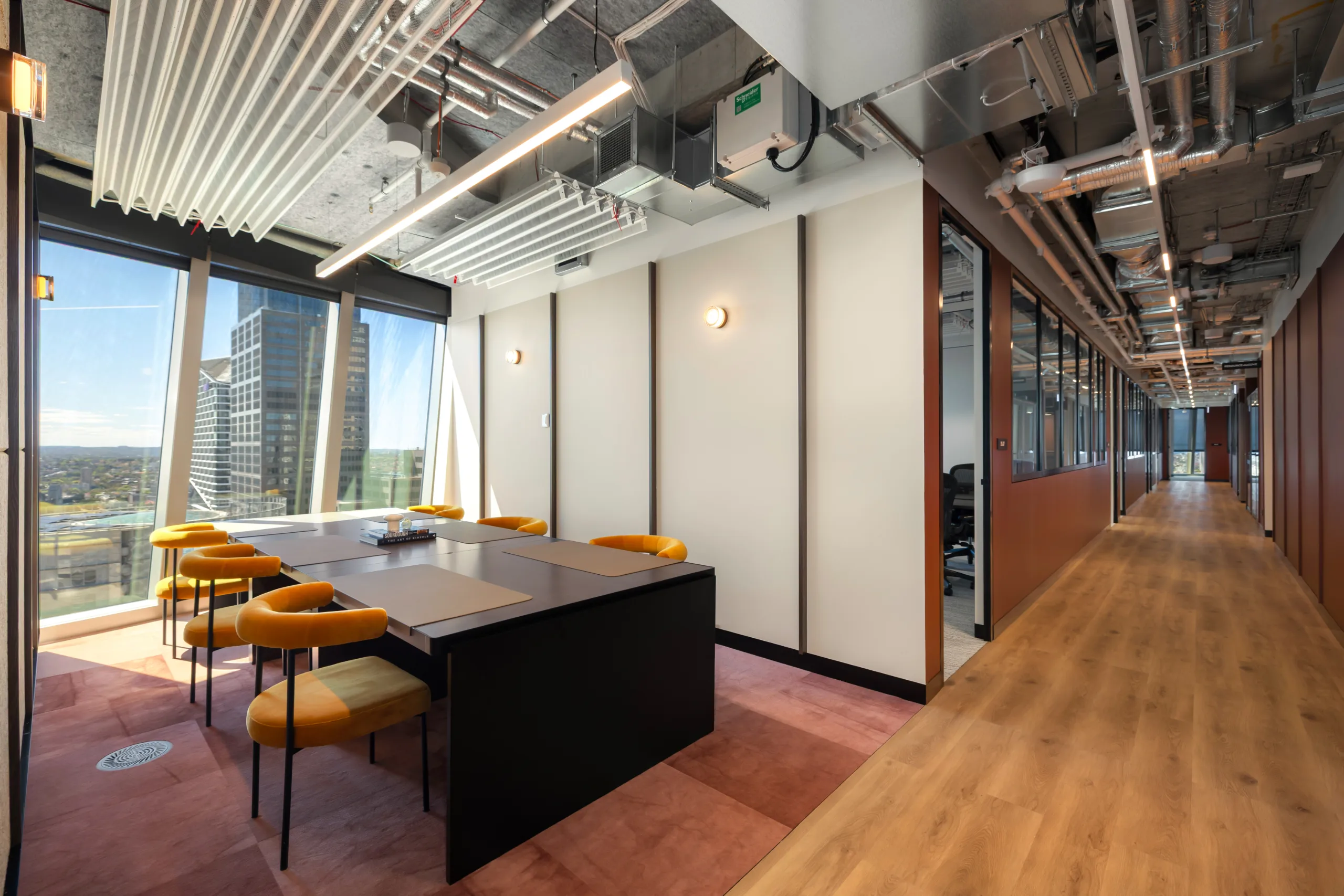 Modern office meeting room with a large black table, yellow chairs, and large windows overlooking city buildings.