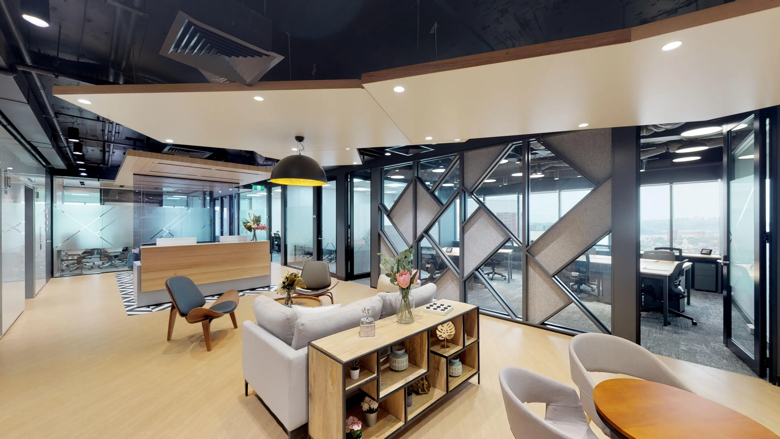 Modern office lounge area with light wood flooring, comfortable seating, and large windows overlooking the city.