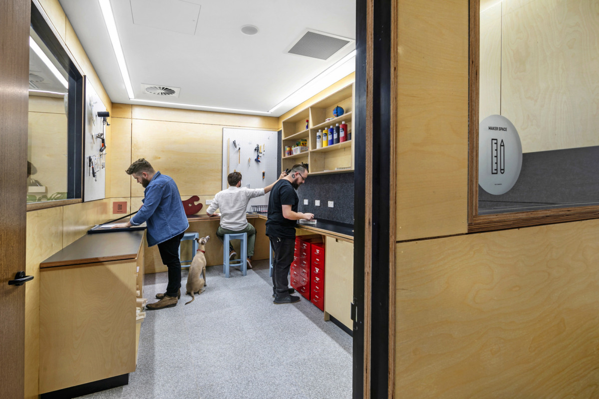 Bright maker space with wooden walls, workbenches, shelving, and people working at various stations.