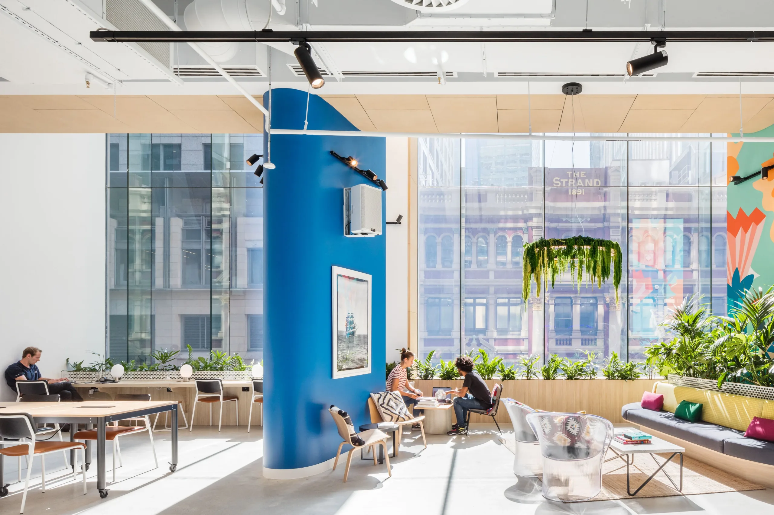 Bright, modern office lounge with large windows, colourful murals, and comfortable seating areas.