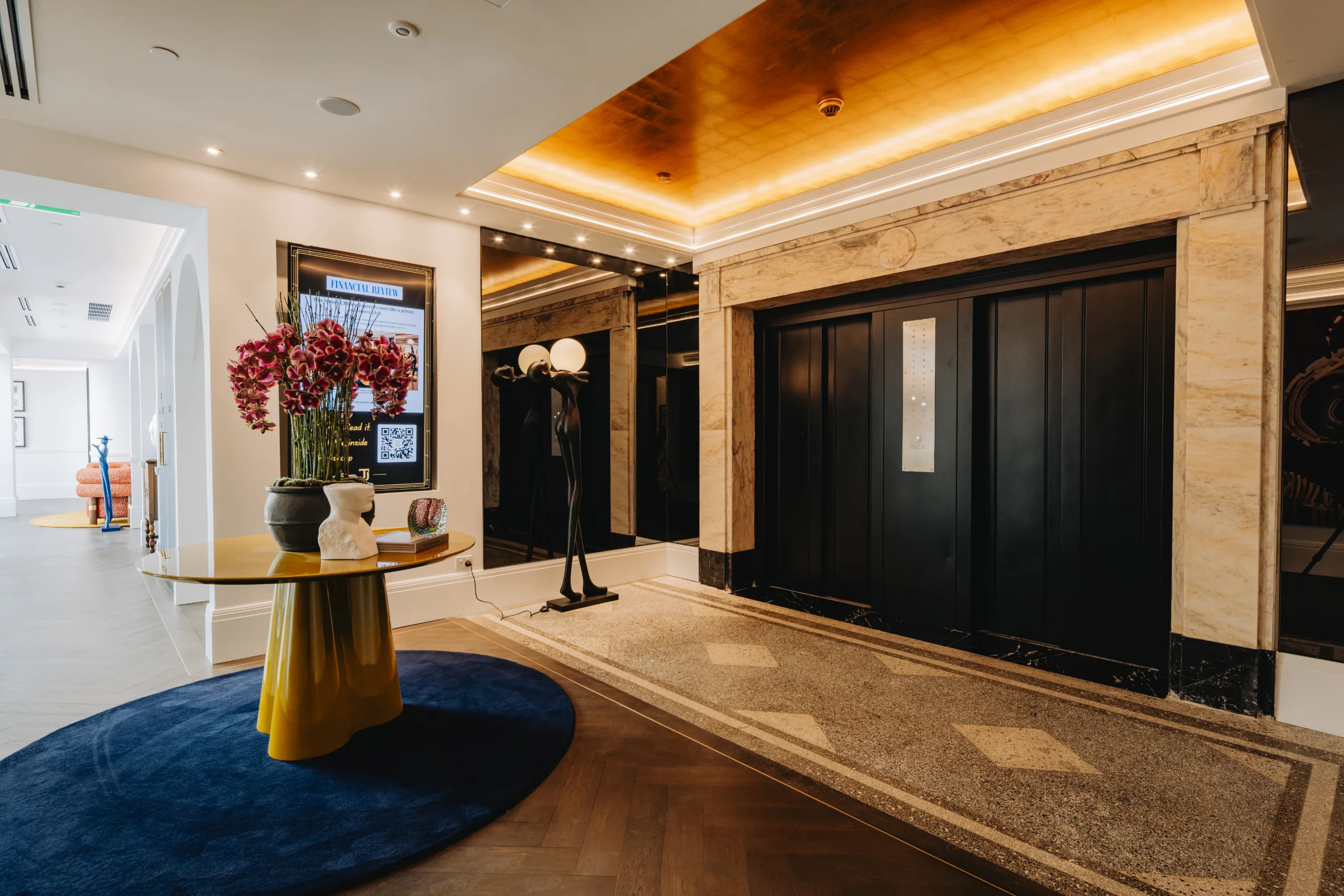 Modern office lobby featuring a gold ceiling, marble walls, and a small round table with pink flowers.