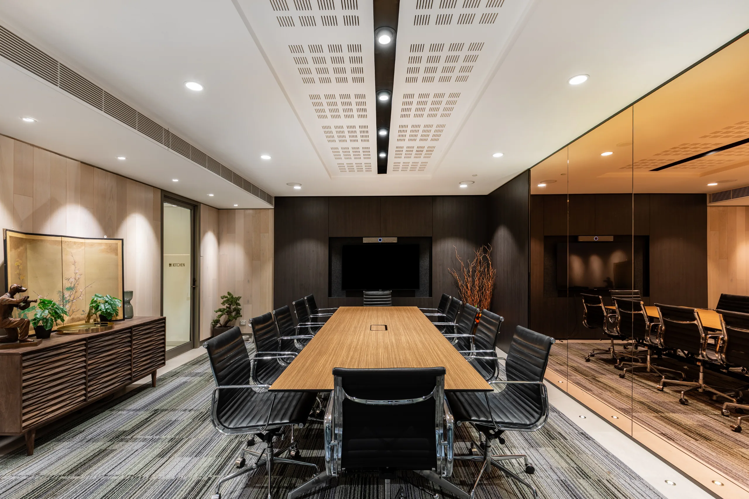 Modern conference room featuring a long wooden table, black leather chairs, and bright recessed lighting.