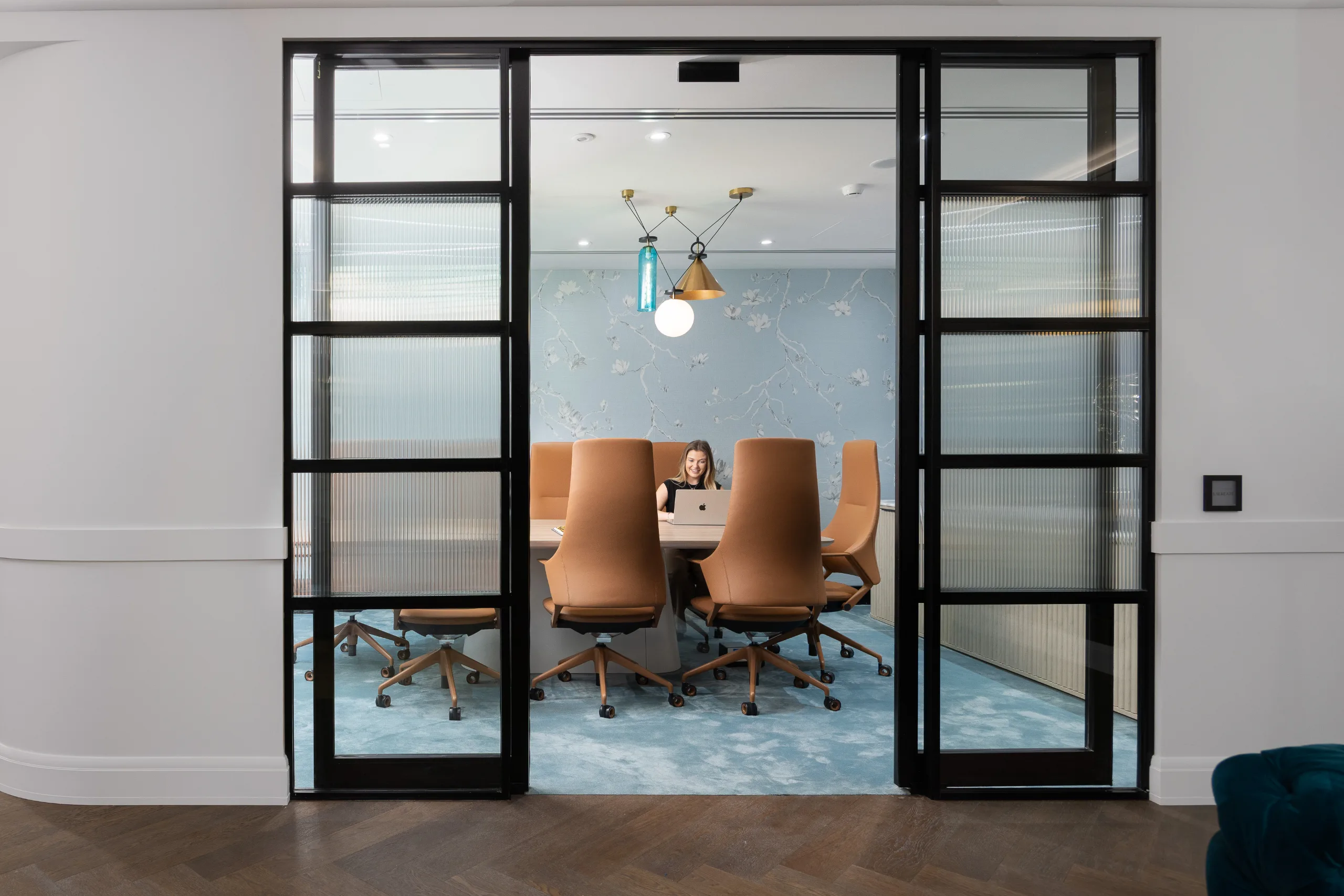 A bright meeting room with floral wallpaper, tan chairs, and large glass sliding doors.