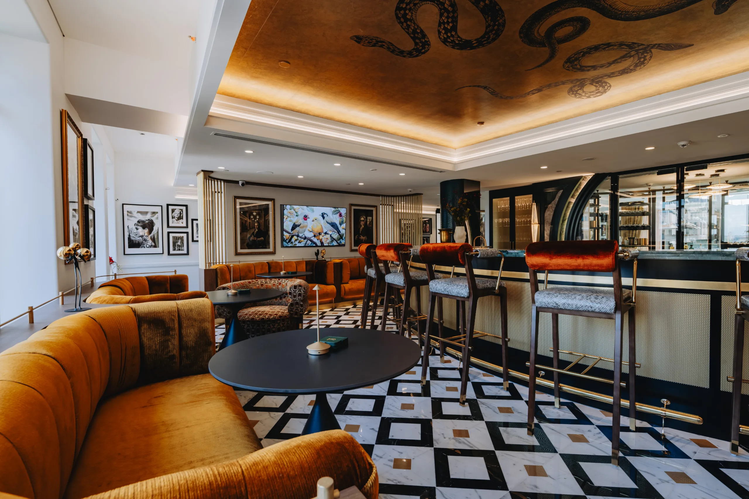 Modern lounge area with velvet seating, a marble checkered floor, and a gold ceiling with snake motifs.
