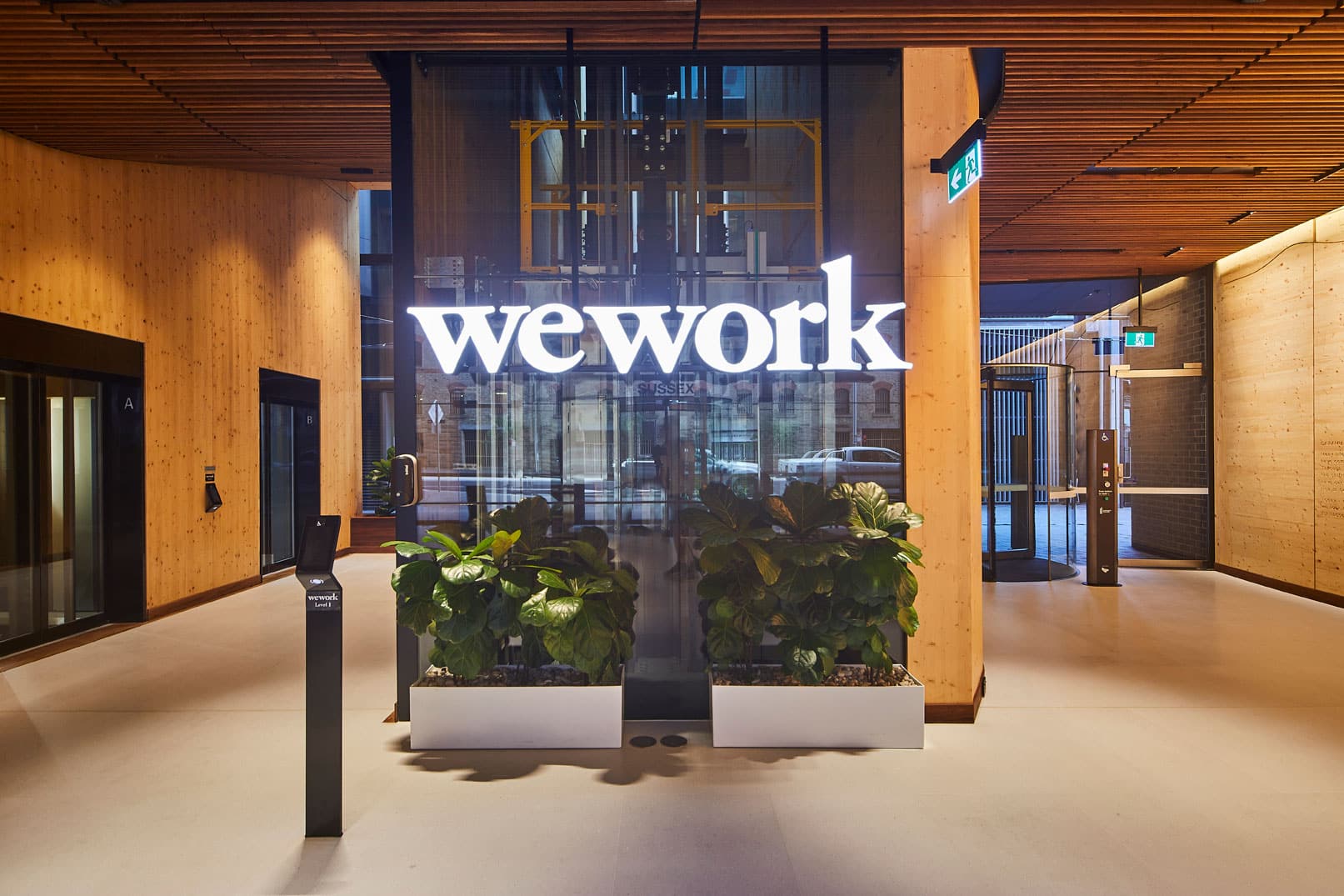 Modern office entrance featuring a large glass wall with a WeWork sign and indoor potted plants.