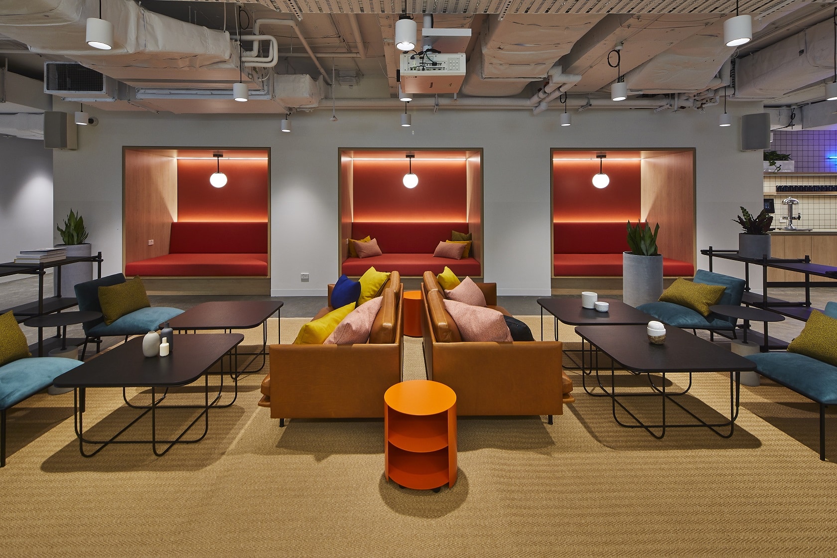 Modern office lounge featuring colourful sofas, small coffee tables, and three recessed red seating alcoves.