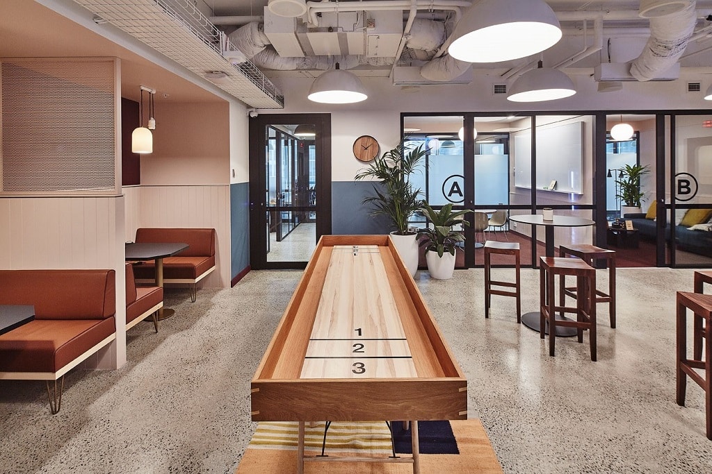 Modern office breakout area featuring a wooden games table, booth seating, and bright overhead lighting.