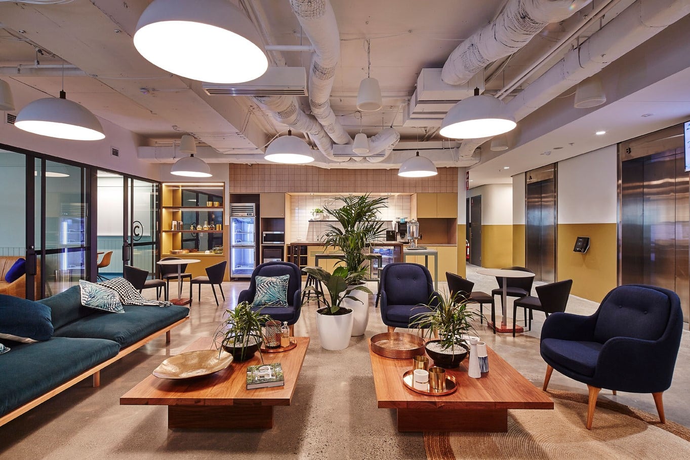 Modern lounge area with navy blue armchairs, wooden coffee tables, and bright pendant lighting.