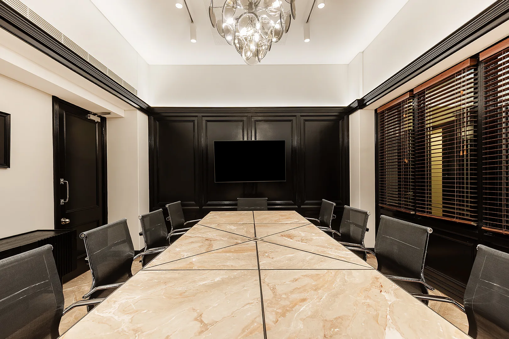 Modern conference room featuring a long marble table, black chairs, and a large wall-mounted television.