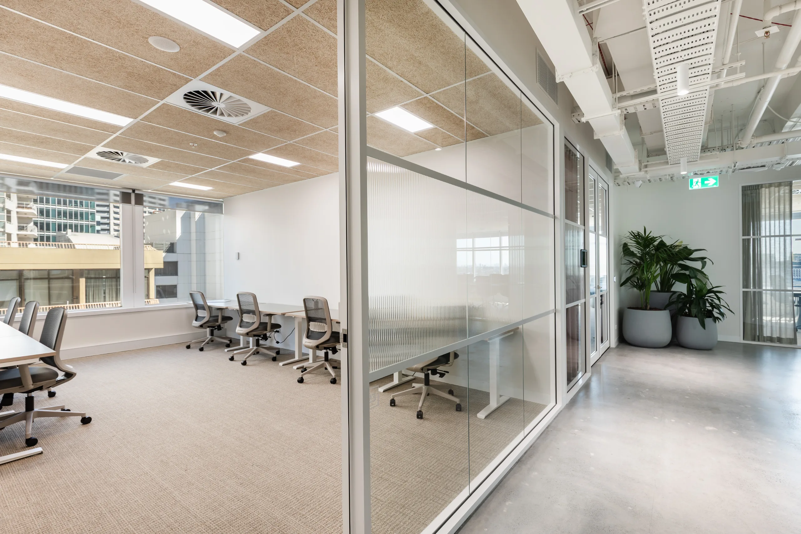 Bright office space with desks, ergonomic chairs, and large windows overlooking city buildings.